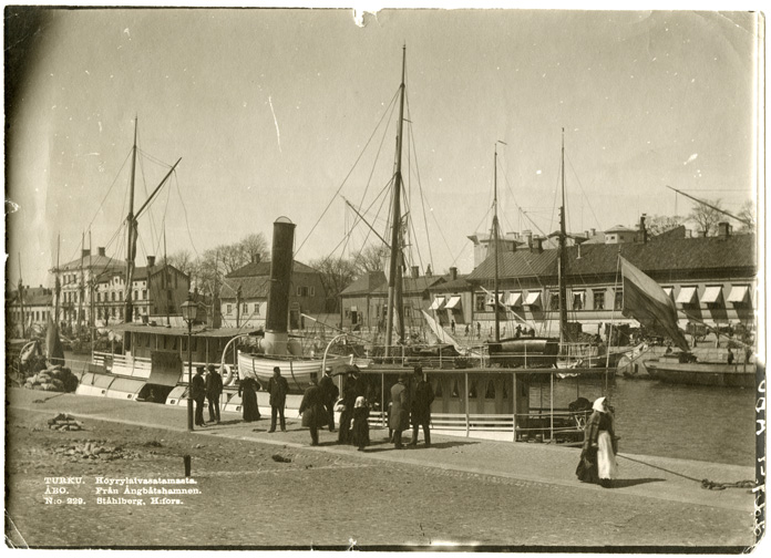 "Från Ångbåtshamnen" Resenärer står på kajen vid en ångbåt i Övre ångbåtshamnen vid Aura å, Åbo.