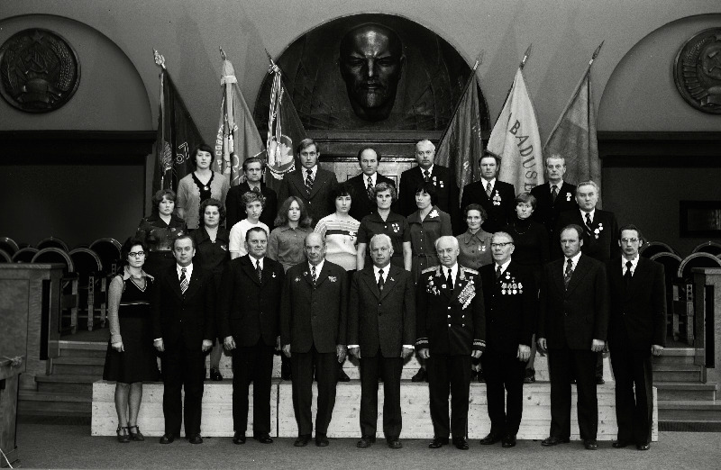 Sidetöötajate, sotsialistliku võistluse võitjate pildistamine revolutsiooni-, lahingu- ja töökuulsuse lippude juures Eesti NSV Ministrite Nõukogu Valges saalis seoses Suure Sotsialistliku Oktoobrirevolutsiooni 60. aastapäeva tähistamisega. Pärnu Rajooni Sidesõlme ülem Endel Tuisk, Vabariikliku Televisiooni Saatekeskuse vaneminsener Mati Tähemaa, Tallinna Kesktelegraafi telegrafist Aino Viigimäe, Viljandi Rajooni Sidesõlme operaator Ene Ilves, Rakvere Rajooni Sidesõlme operaator Taimi Kurg, Tallinna Peapostkontori operaator Katrin Lee, Pärnu Rajooni Tõstamaa Sidesõlme ülem Leopold Lõpp,    jätkub: Kohtla-Järve Rajooni Sidesõlme postiljon Galina Merkulova, Pärnu Ekspluatatsiooni - Tehnilise Sidesõlme elektrimontöör Tiit Metsallik, Harju Rajooni Sidesõlme telefonist Marika Raiend, Narva Linna Sidesõlme telefonist Antonina Rubanova, Paide Rajooni Sidesõlme operaator Elvi Saad, Ajakirjanduslevi Pärnu Rajooni agentuuri kiosköör Asta Sukk, Kingissepa Rajooni