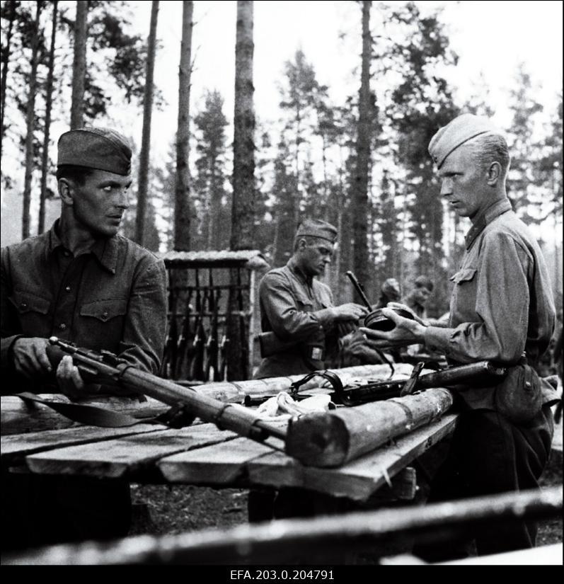 Stseen Tallinnfilmi mängufilmist "Inimesed sõdurisinelis". Sõjamehed tegelevad relvadega. Esiplaanil Kalm (Rudolf Allabert) ja Agur (Tõnu Mikiver).