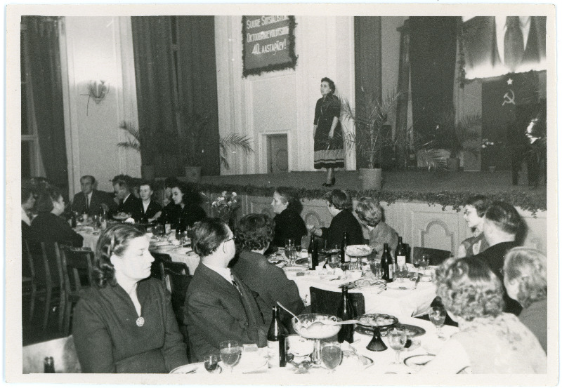 Suure Sotsialistliku Oktoobrirevolutsiooni 40.aastapäeva üritus Sakala keskuses 1958, laval esineja (kõneleja), saalis istuvad inimesed kaetud laudade taga. Ajakirja Nõukogude Naine peatoimetaja Magda Korb istub seljaga lava poole, vasakult kolmas