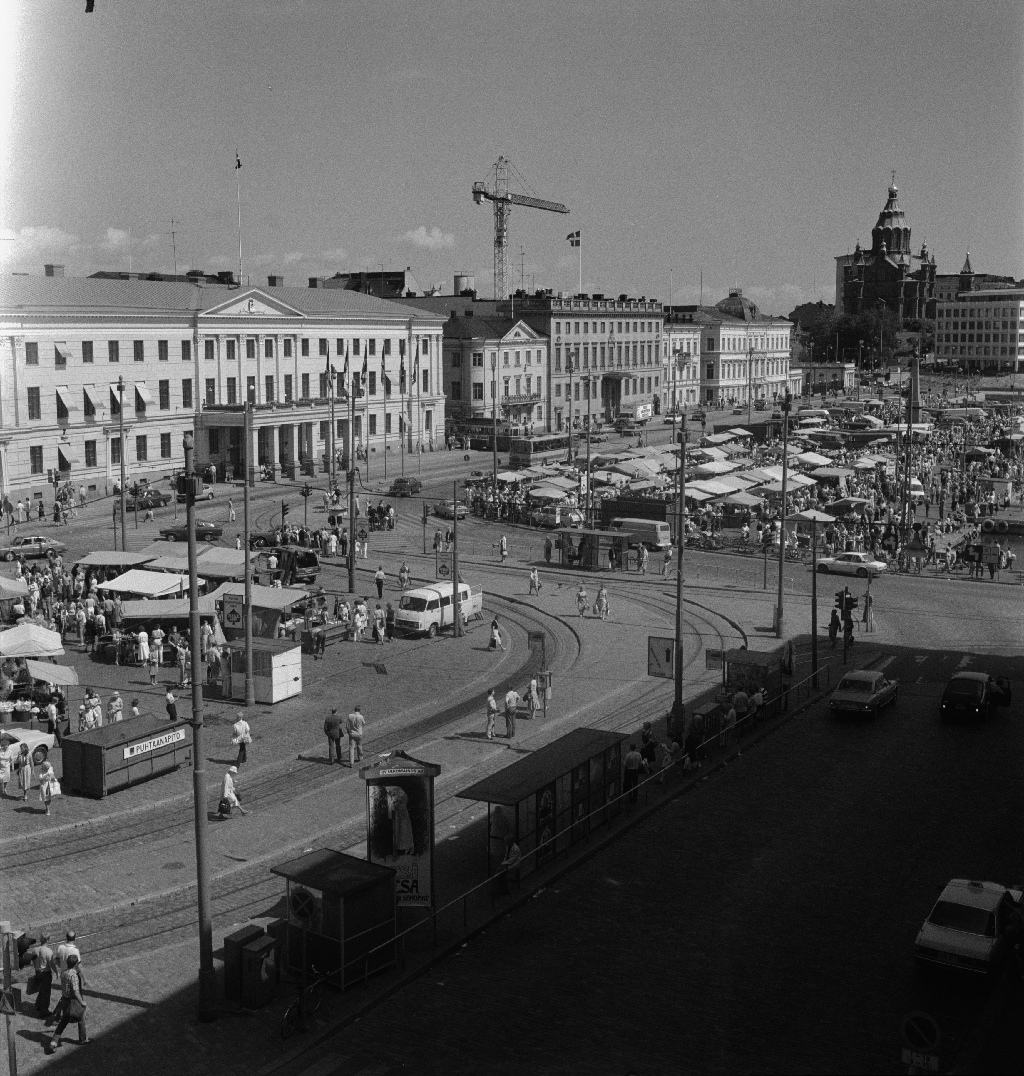 {'fi': 'Kauppatori', '_type': 'lang'} - Kauppatori. Vasemmalla Pohjoisesplanadi 11-13, 9, 7, 5, 3. Taustalla Katajanokalla Uspenskin katedraali. -- negatiivi, filmi, mv