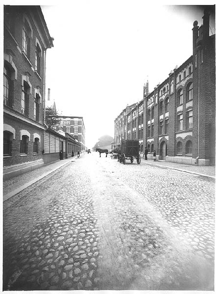 Exteriör: Aktiebolaget John Barkers textilfabriks fasad på Slottsgatan. Fasaden mot Slottsgatan är nygotik i tegelsten, gatan är kullerstensbelagd. Framför ingången står en häst med en transportvagn. Barkers var ett bomullsspinneri, väveri, färgeri och bl