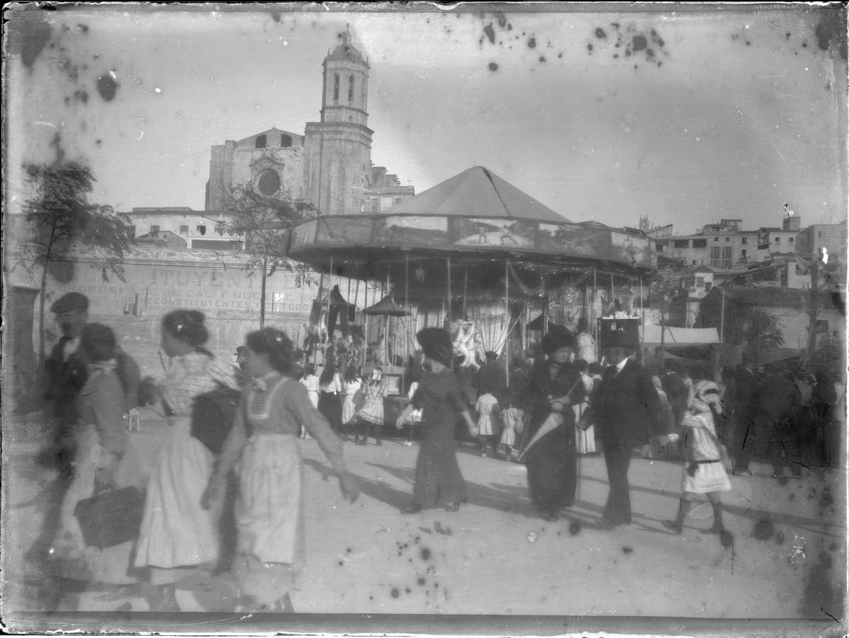 [Attractions of the Fairs and Festivals of St. Narcissus] - Attraction of fairs in St. Augustine Square. The fairs were held in this place from 1900 to 1922, when it was decided to move the attractions Ramon Folch Avenue. In St. Augustine Square there are only stops. In 1932, as a result of the celebration of the 1st Trade Fair Avenue Ramon Folch, fairs are located along the Gran Via. It was not until 1960 when they moved permanently to the Dehesa. In the background is the Cathedral with the image offered before the completion of the facade, and below, an announcement of a reconstituent painted on the wall that closed the square on the side of the river, the bottom of which still retains features of the fortification facing the Onyar. The wall desparagué 1914 with the development of the Paseo Canalejas.