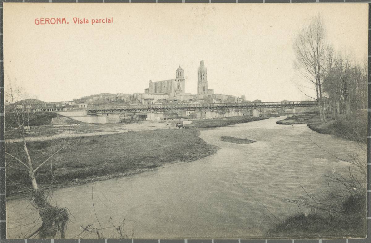 Gerona. Partial view - The confluence of the Ter and Onyar rivers, at the height of the railway bridge There is a carriage circulating on the Pedret’s sidewalk, covered by the waters. In the centre, the Cathedral of Girona and the bell church of Sant Feliu. In the background to the right, the footbridge Portal de la Barca.