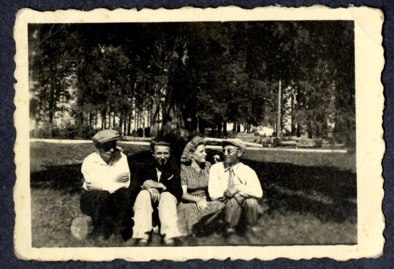 Neiu ja kolm noormeest istuvad pargis või puudesalus palgi peal