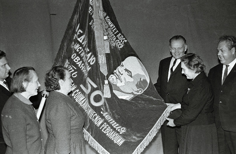 Kolhoosi Estonia (vasakult) lüpsja-karjatalitaja, kahe Lenini ordeni omanik H. Mäsak, sotsialistliku töö kangelased lüpsja-karjatalitaja E. Mihkelson, majandi esimees H. Marrandi ja farmijuhataja P. Käsper ning EKP Keskkomitee teine sekretär A. Vader Suure Sotsialistliku Oktoobrirevolutsiooni 50. aastapäeva eelse sotsialistliku võistluse võitjatele antud mälestuslipu juures.