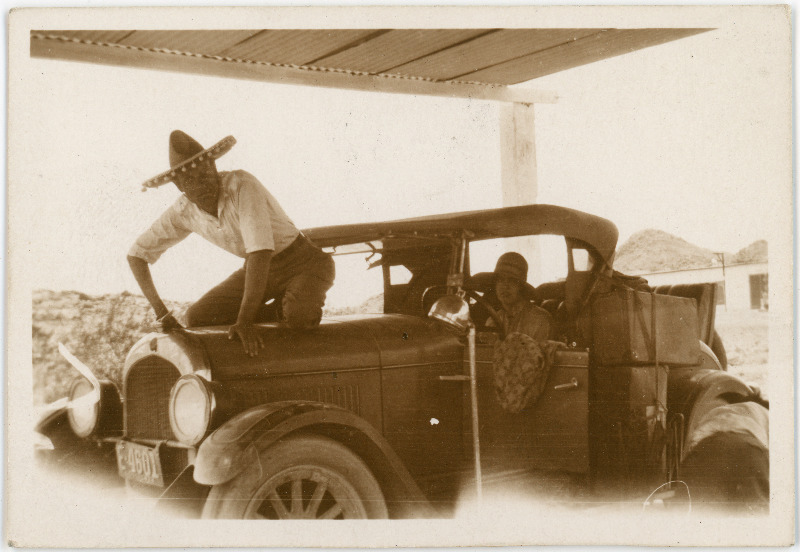 Tundmatu paar autoga - naine rooli taga, mees, sombreero peas, poseerimas auto kapotil