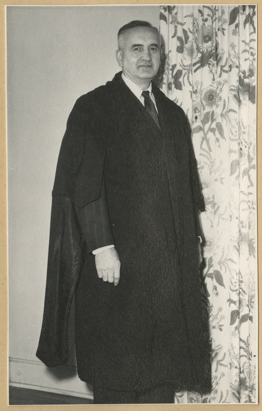 Tumedas ülikonnas mees seismas toas akna juures