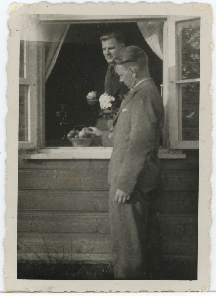 Kaks noormeest akna juures, üks väljas, teine toas