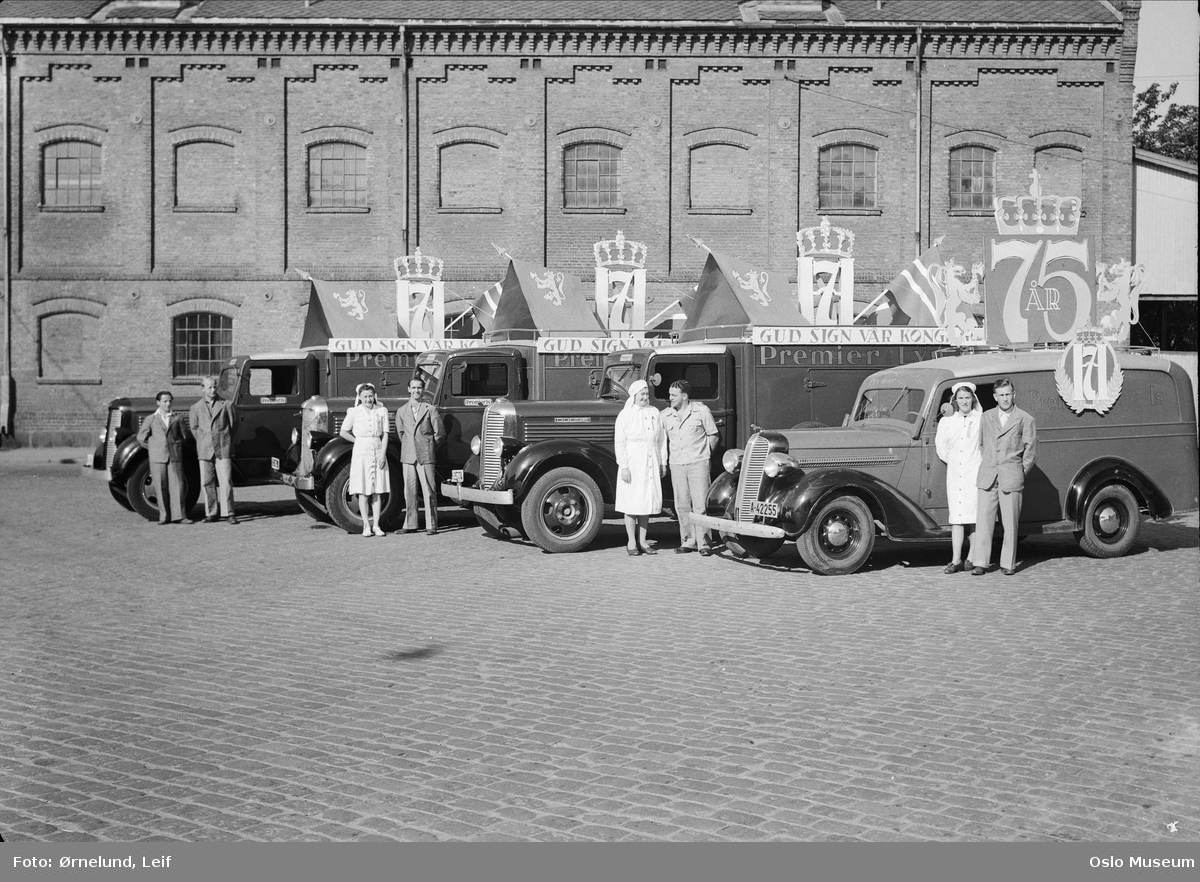 Tre Dodge lastebiler årsmodell 1937-38. Nærmest Dodge 1936 varebil., Premier Is iskremfabrikk, varebiler med kongebanner i anledning Haakon VIIs 75-årsdag, menn, kvinner