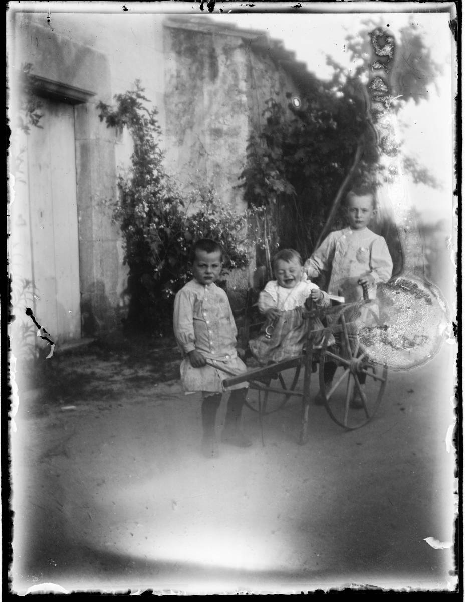 [Children by car] - Portrait of three children with a cart.