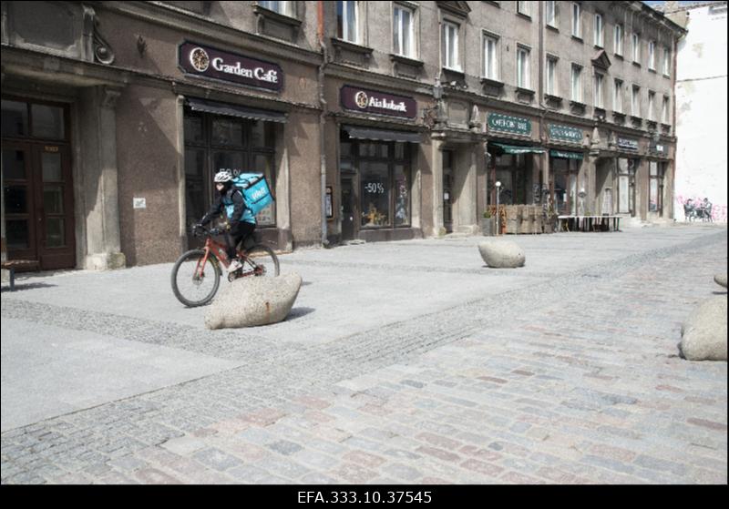 Vaade inimtühjale Kullassepa tänavale koroonapandeemia ajal.  Keskel jalgrattal Wolt toidukuller.
