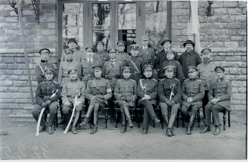 Vabadussõda. Sõjakooli juhtkond, lektorid ja külalised kooli hoone ees Tehnika tänaval. Vasakult: I rida - 1.taktika lektor ja kadettide jalaväeroodu ülem kapten Ludvig Jakobsen, 2.kooli ülem kapten Aleksander Simon, 3.tundmatu Ameerika Ühendriikide ohvitser, 4.sõjaministri abi ja tagavaravägede ülem kindralmajor Andres Larka, 5.Kindralstaabi ülem alampolkovnik Jaan Rink, 6.kooli klasside inspektor alamkapten Heinrich Paavijaan (Hendrik Pallandi), 7.topograafia lektor ja Sõjaväe Korraldusvalitsuse topograafiaosakonna ülem alampolkovnik Eduard Bach, 8.fortifikatsiooni lektor ja Inseneripataljoni ülem kapten Voldemar Riiberg (Rieberg); II rida: 1.kooli adjutant alamleitnant Magnus Siiak, 2.[taktika lektor ja jalaväekadettide 2.rühma ülem alamleitnant Richard Kent], 4.[raadiosidelektor alamleitnant Friedrich Olbrei] 5.kuulipildujate materjalosa lektor ja Kaitseliidu staabi ohvitser leitnant Albert Murrik, 6.lõhkeainete lektor ja Sõjaväe Korraldusvalitsuse inspektorijaoskonna ülem alamkapten August Steinberg, 7.telegraafiside lektor ja Kindralstaabi Valitsuse maakuulamise (luure-) osakonna ülem alamleitnant Arthur Perna (Artur Pärna); III rida: 3 .ratsaklassi ülem kapten Alfons Parisson (Parison), 6.[eesti keele lektor Karl Pinkowski?].