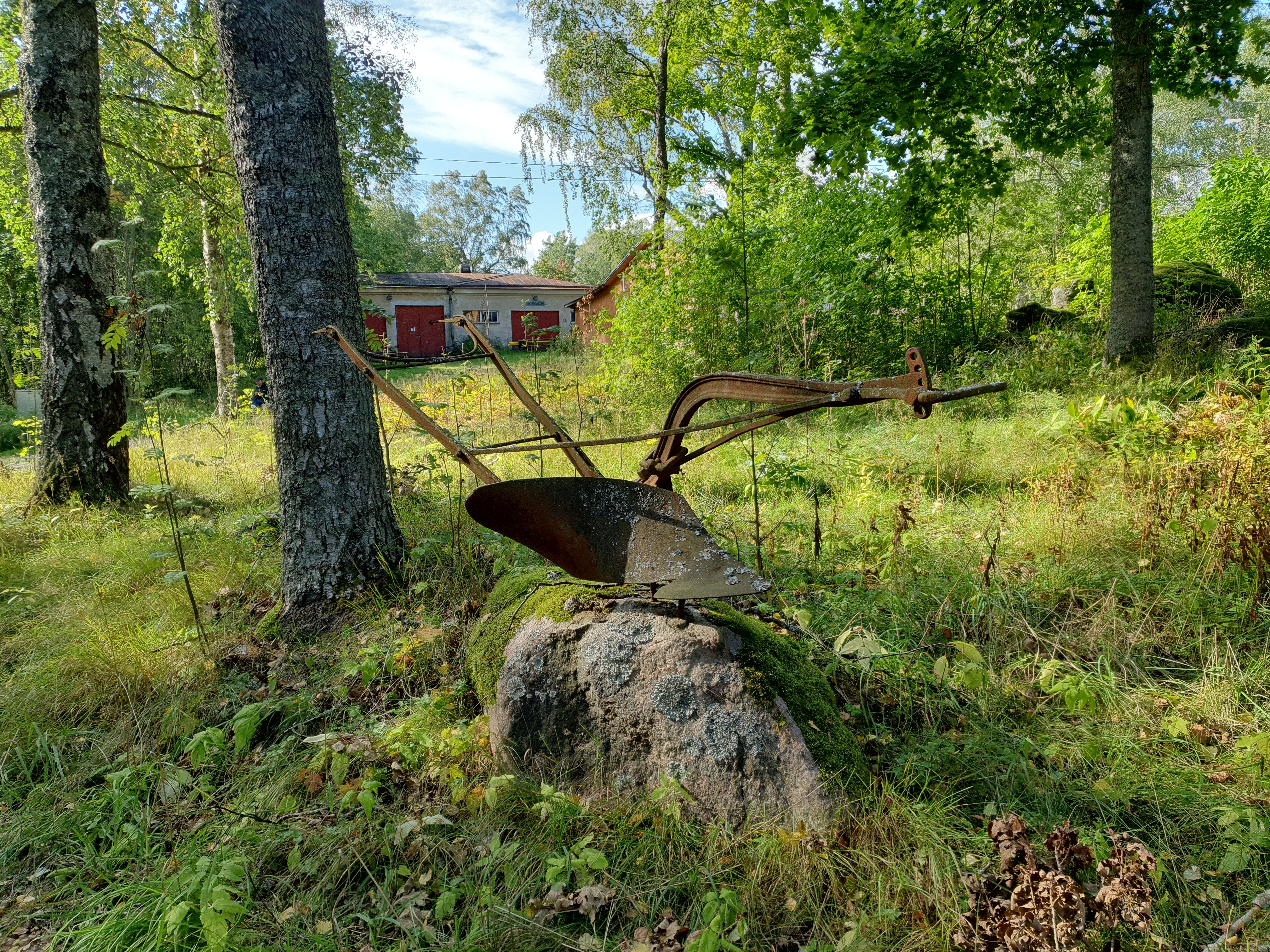 Vanha ruosteinen aura kivellä Vallisaaressa. Taustalla avautuu näkymä paloaseman pihapiiriin. Vasemmalla näkyvä punaovinen rakennus on palokalustovaja, jossa säilytettiin aikanaan T-mallista Fordia, kuorma-autoa ja hevosvetoisia kärryjä. Sitä vastapäätä oikealla näkyy puusepänverstas. rephoto