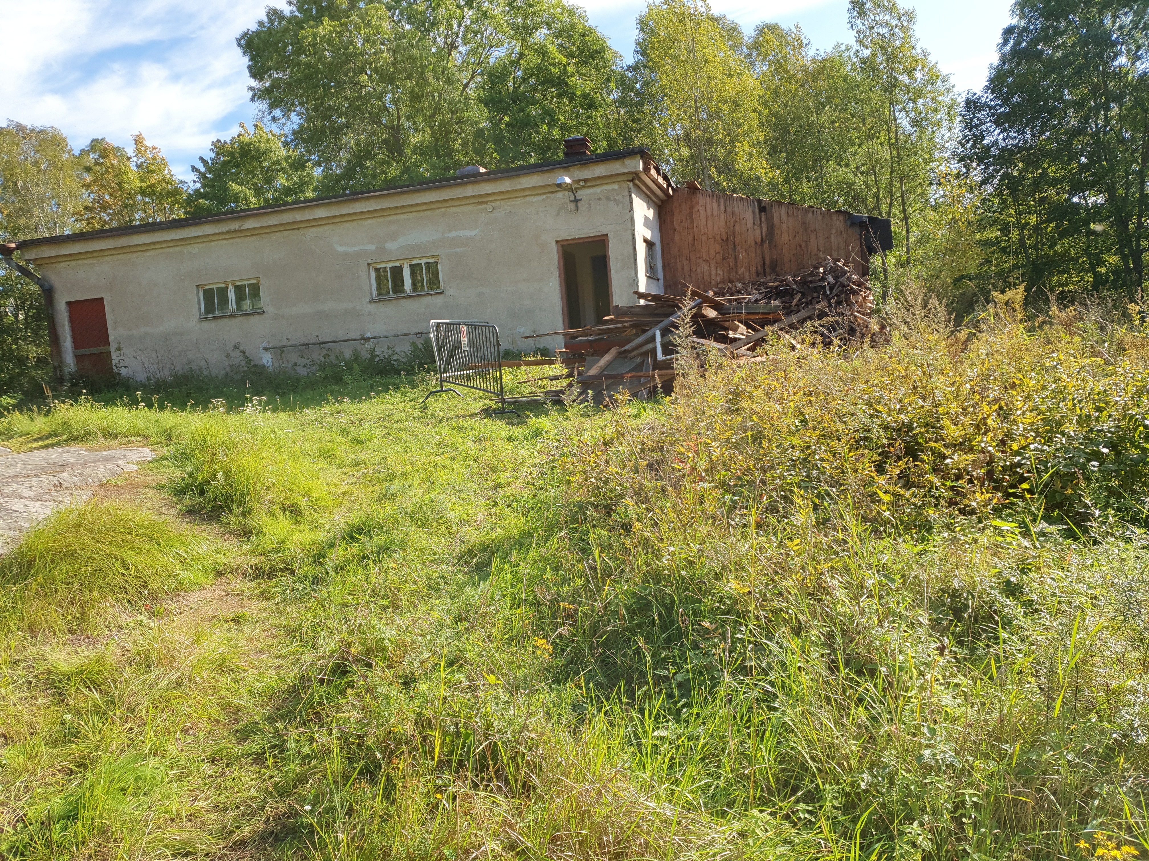 Paloaseman palokalustovaja Vallisaaressa. Siinä säilytettiin aikanaan T-mallista Fordia, kuorma-autoa ja hevosvetoisia kärryjä. Keskimmäisestä ovesta kuljettiin kahden hevosen talliin ja viereisestä punaisesta ovesta hevosten rehu- ja heinävarastoon. Pihapiiriin kuuluu myös vasemmassa reunassa näkyvä puusepänverstas. Valokuva on otettu aurinkoisella säällä. rephoto