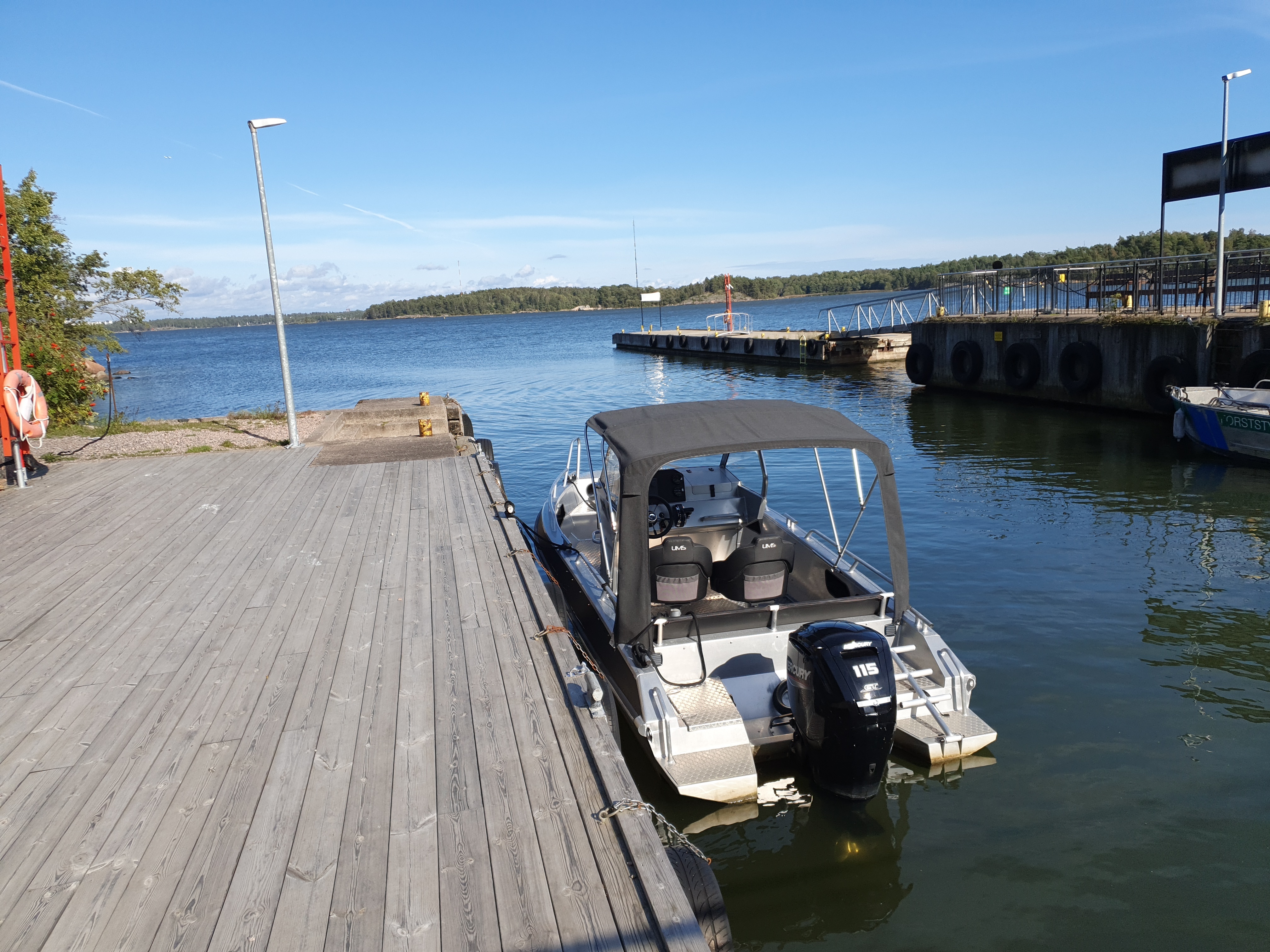 Retkeläiset menossa taksiveneeseen Vallisaaressa. Paikka on Torpedolahden laituri Vallisaaren itärannalla. Taivaanrannassa Haminansalmen toisella puolen näkyy Santahamina. rephoto