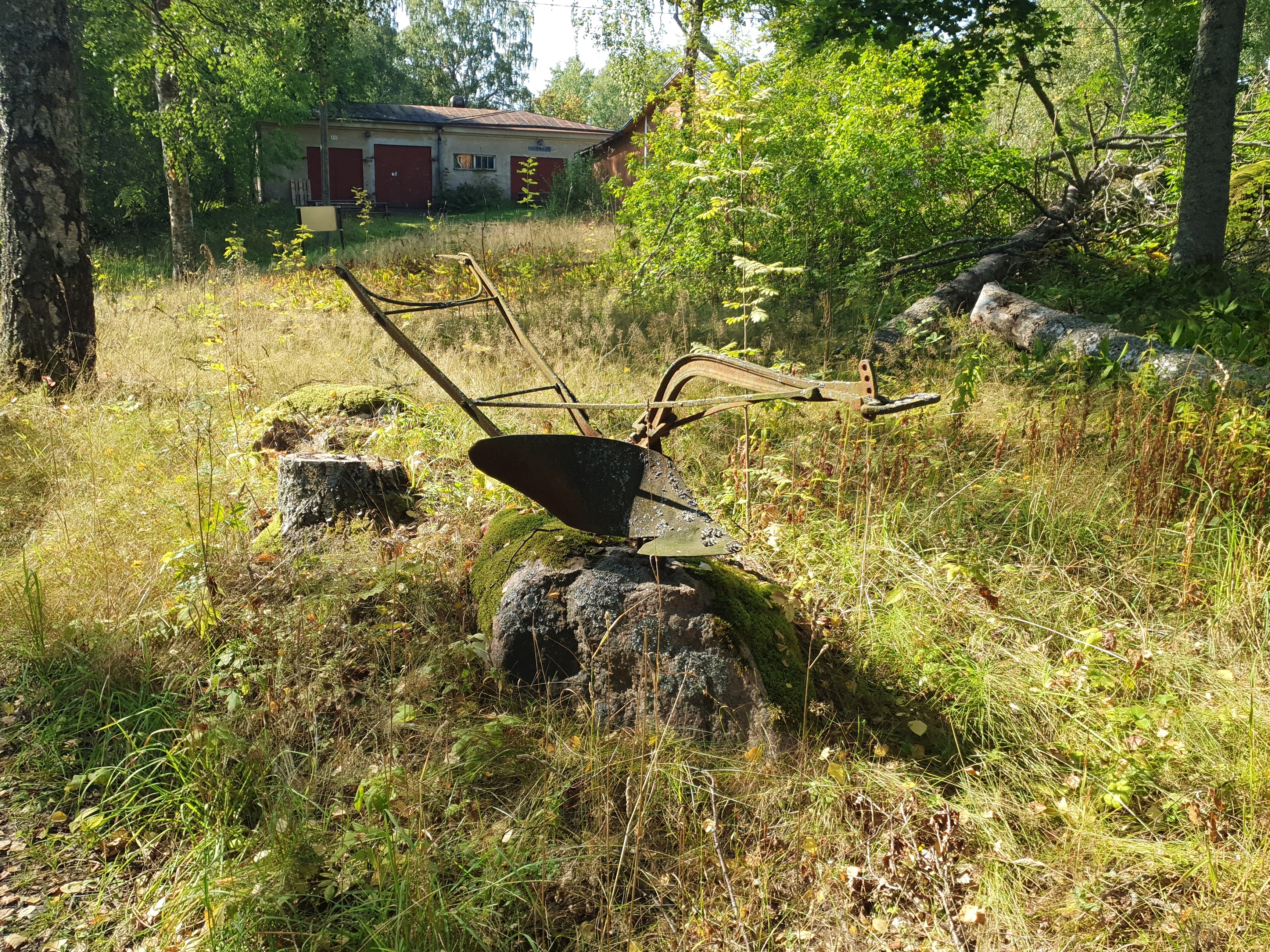 Vanha ruosteinen aura kivellä Vallisaaressa. Taustalla avautuu näkymä paloaseman pihapiiriin. Vasemmalla näkyvä punaovinen rakennus on palokalustovaja, jossa säilytettiin aikanaan T-mallista Fordia, kuorma-autoa ja hevosvetoisia kärryjä. Sitä vastapäätä oikealla näkyy puusepänverstas. rephoto