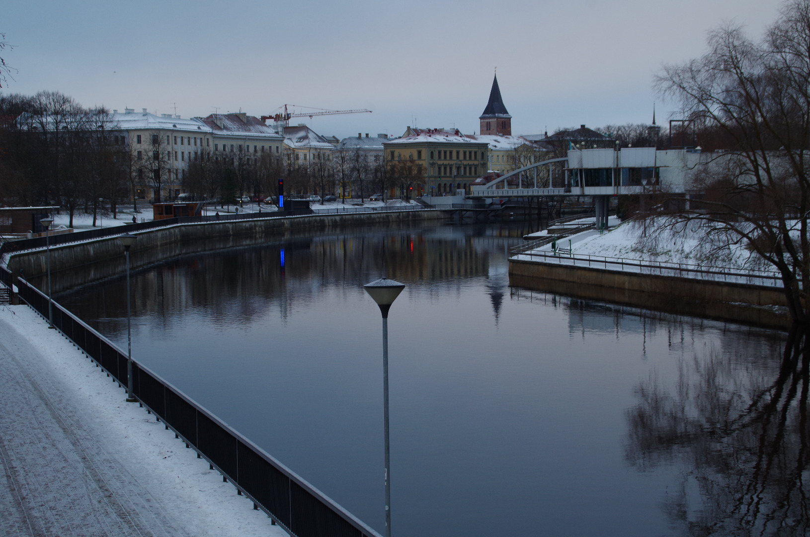 Tartu kesklinn Emajõe parem- ja vasakkaldal. 
Esiplaanil Emajõe üleveoparv Uueturu ja Holmi t joonel. Taga Kivisild.
Paremal hotelli "Jakor" hoone ( juugendstiil, arh. R. von Engelhardt, 1905), eemal kino "Illusion" hoone. Vasakul lodjad. 
Tartu, ca 1910. rephoto