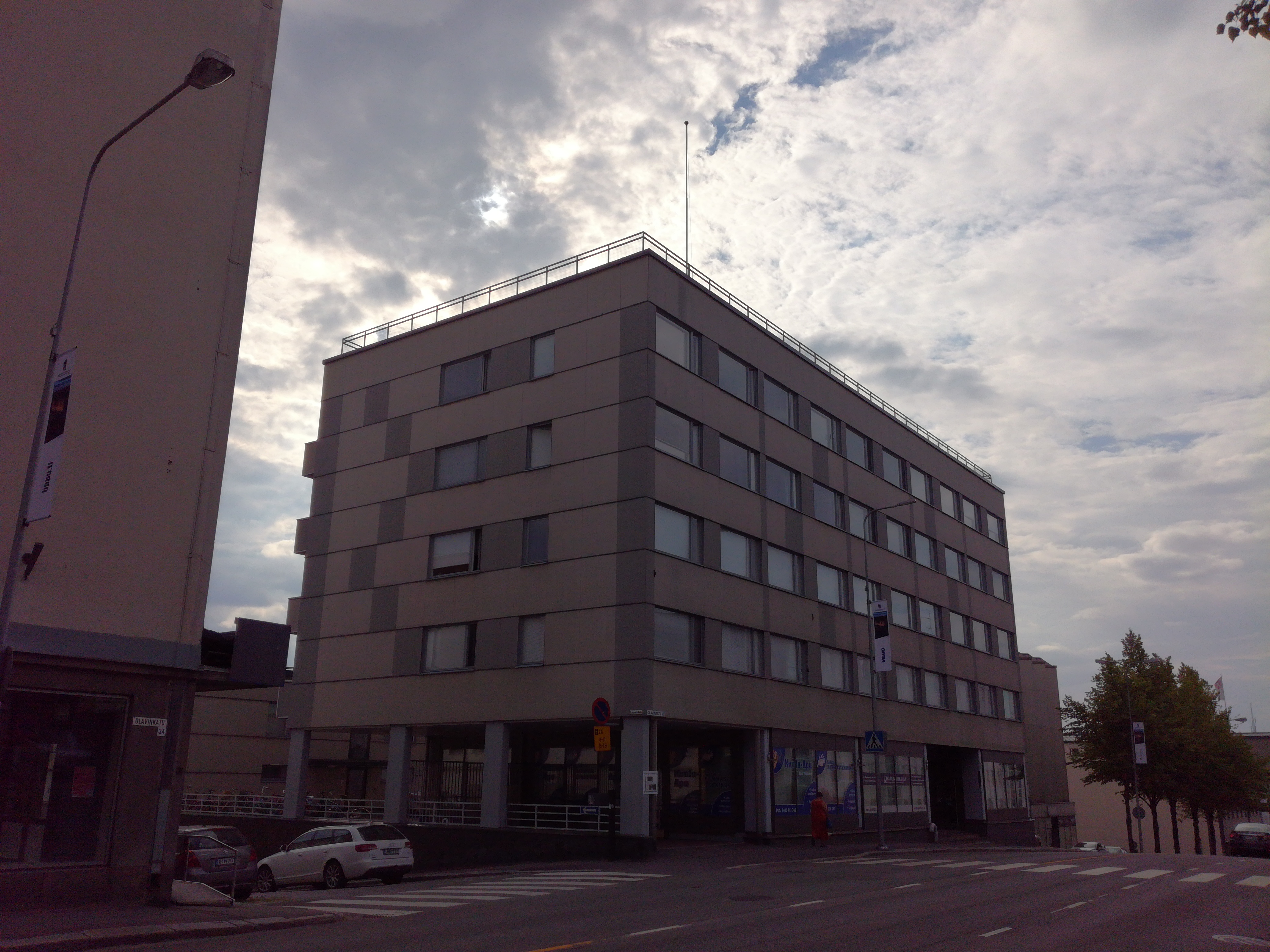 Entinen raatihuone, myöhemmin posti (Olavinkatu 36) idästä Olavinkadun yli. Olavinkatu 34:n kohdalla puuaidassa mainoskaappeja, katu mukulakivipäällysteinen, kangaskattoinen auto, jalankulkijoita. Takana oikealla And. Auvisen rakennus (Olavinkatu 38). rephoto