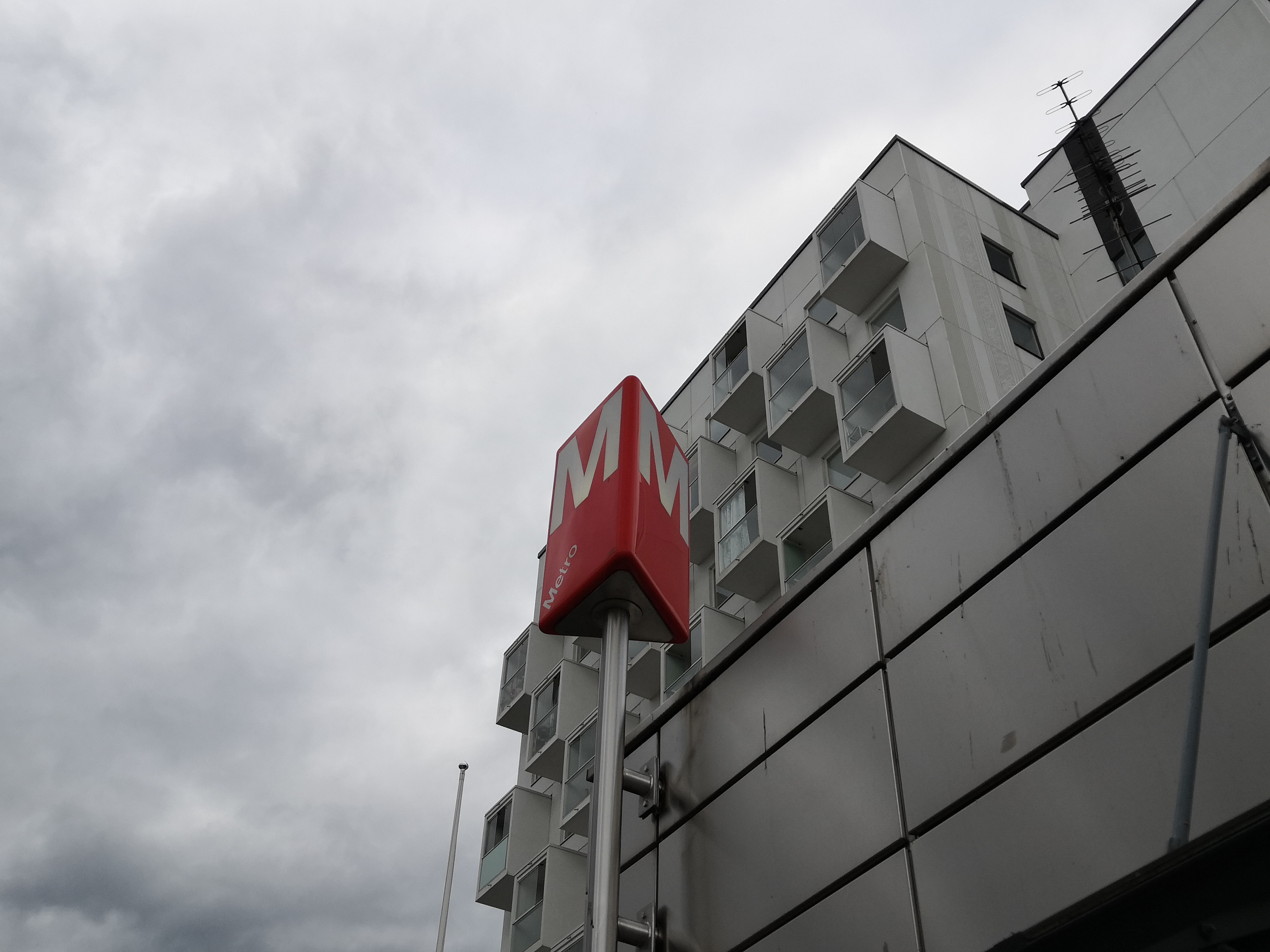 Rastilan metroasema Vuosaaressa. Metroaseman merkki lähikuvassa. Takana asuinrakennus. rephoto
