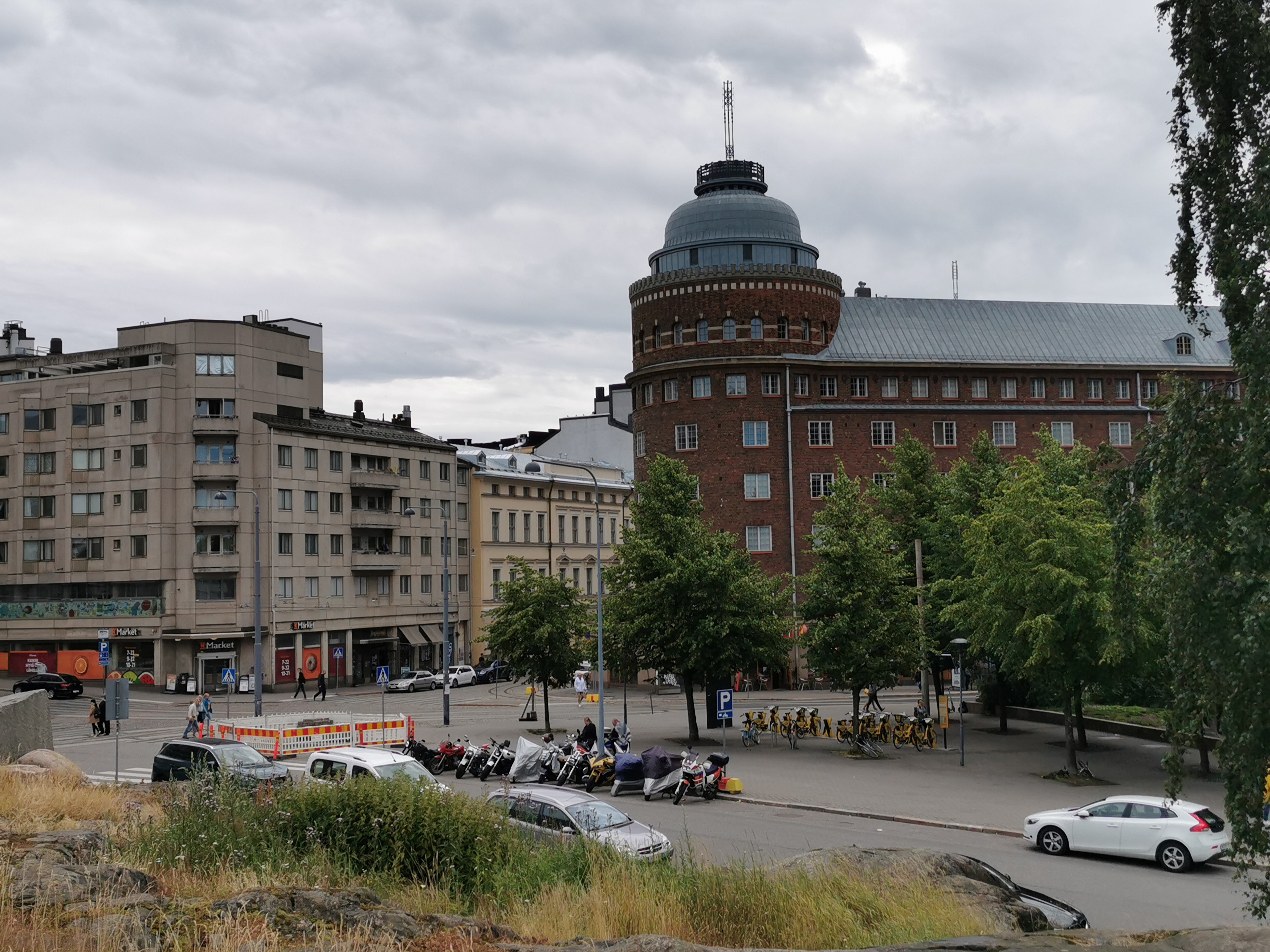 Rakennuksia ja aidattu puutavaran varastointialue nykyisen Ympyrätalon paikalla. Oikealla Porthaninrinne 1 ja 3. Vasemmalla Toinen linja 5 ja Porthaninkatu 1. Taustalla Arena talo. rephoto