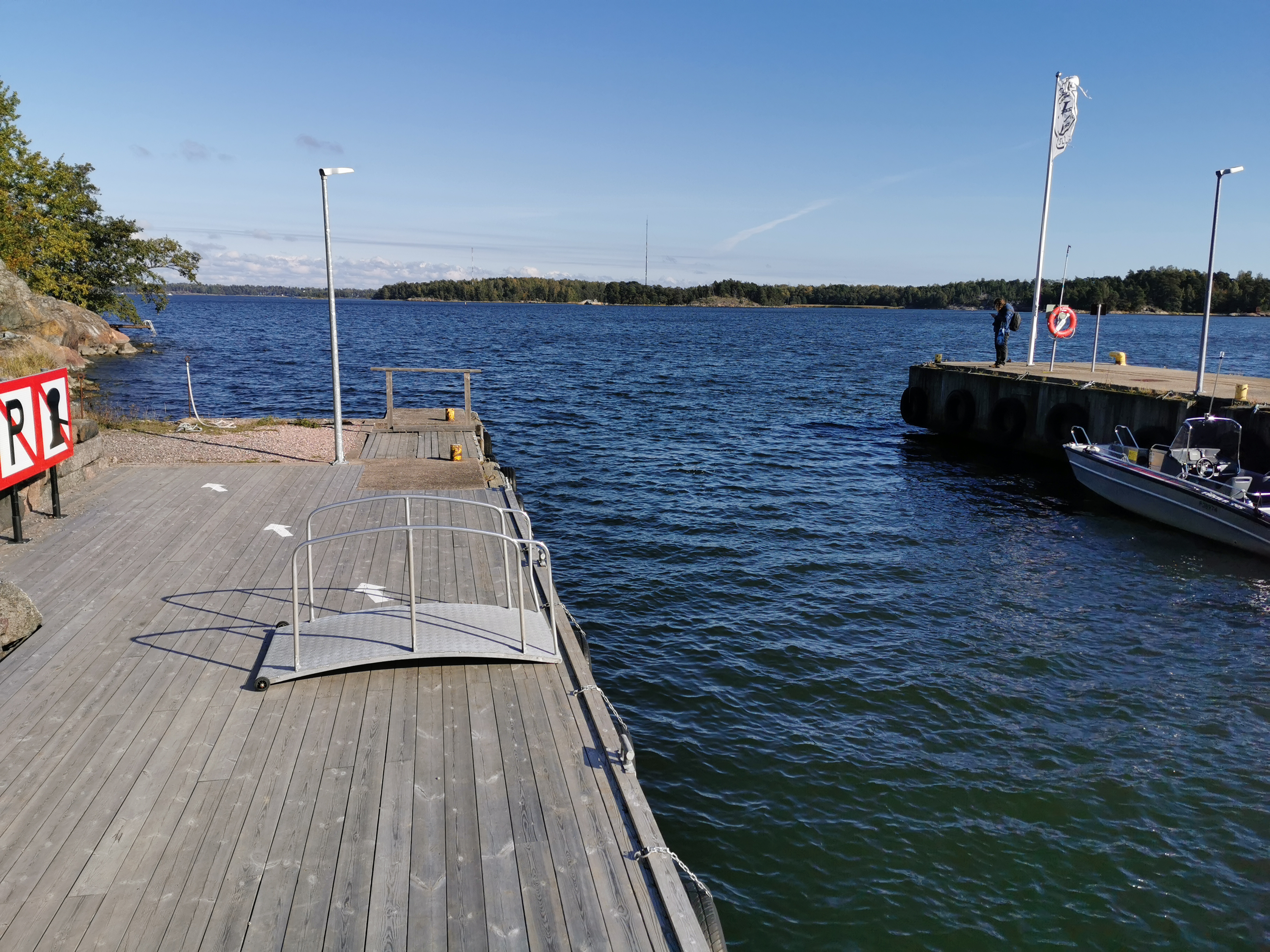 Retkeläiset menossa taksiveneeseen Vallisaaressa. Paikka on Torpedolahden laituri Vallisaaren itärannalla. Taivaanrannassa Haminansalmen toisella puolen näkyy Santahamina. rephoto