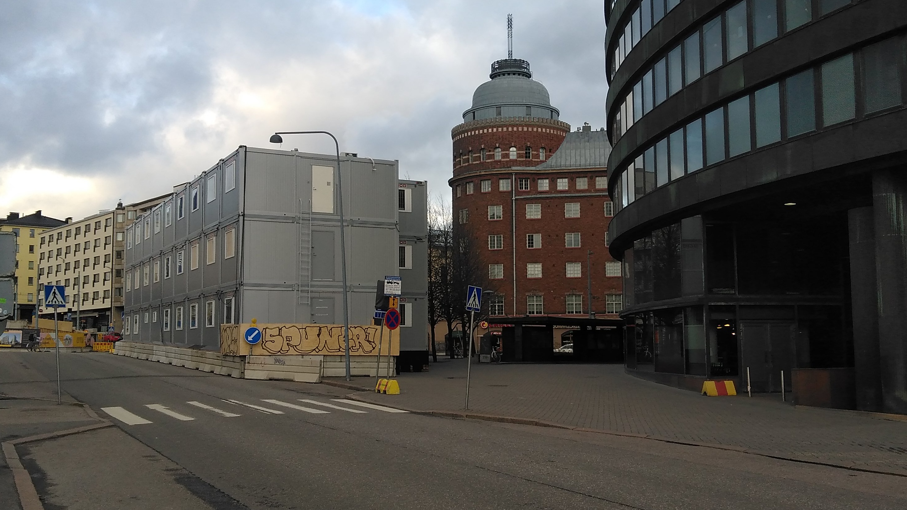 Rakennuksia ja aidattu puutavaran varastointialue nykyisen Ympyrätalon paikalla. Oikealla Porthaninrinne 1 ja 3. Vasemmalla Toinen linja 5 ja Porthaninkatu 1. Taustalla Arena talo. rephoto