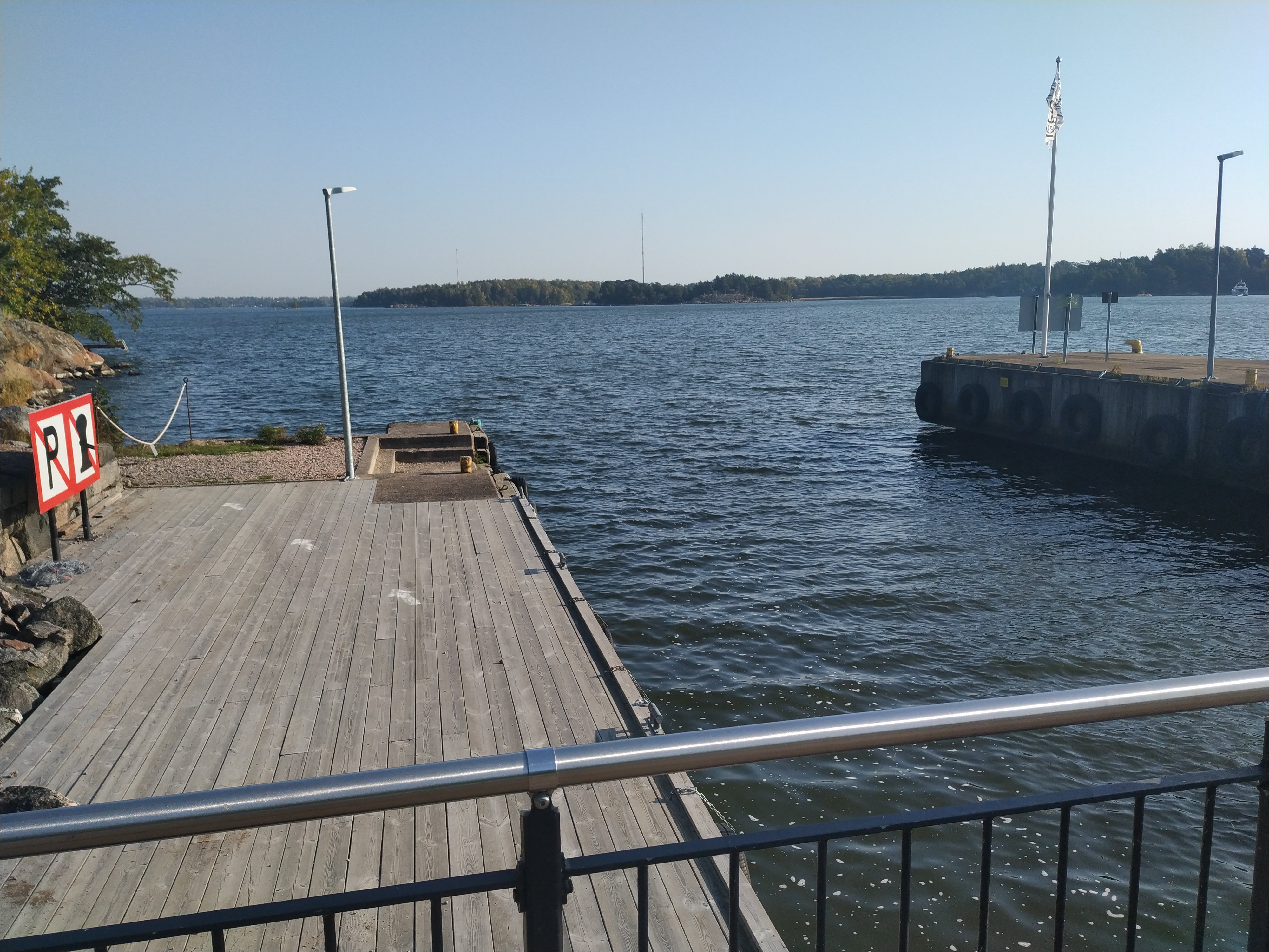 Retkeläiset menossa taksiveneeseen Vallisaaressa. Paikka on Torpedolahden laituri Vallisaaren itärannalla. Taivaanrannassa Haminansalmen toisella puolen näkyy Santahamina. rephoto