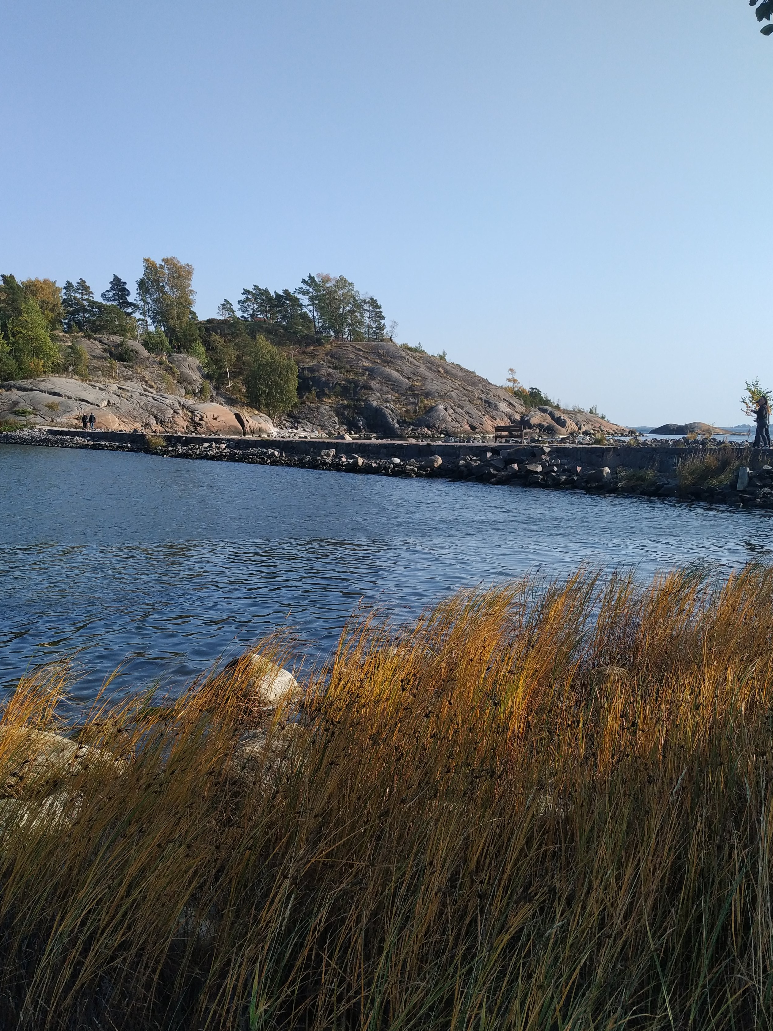 Juhannuskokko Kuninkaansaaren ja Vallisaaren välissä. Kokko on koottu saarten väliin rakennetun vallin päällä kulkevalle tielle. Valokuva on otettu Vallisaaren puolelta siten, että taustalla näkyy Kuninkaansaari. Kokon läheisyyteen on kerääntynyt ihmisiä seuraamaan roihua. rephoto