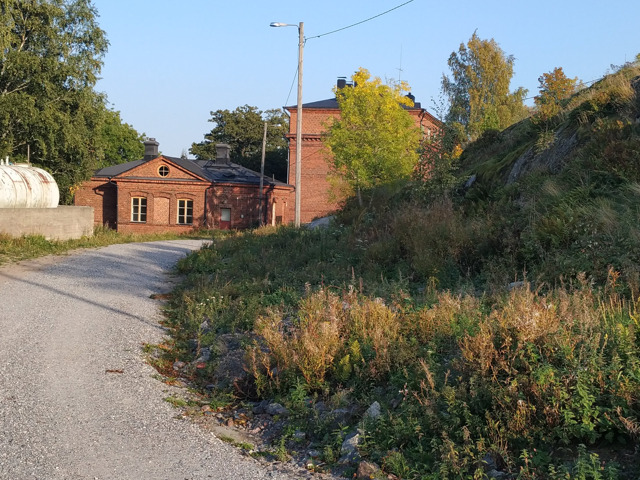 Näkymä Vallisaaresta. Oikealla on luotsitalo ja keskellä näkyy luotsitalon saunan ja pesutuvan rakennus. Vasemmalla alunperin venäläisten varuskuntansa saunaksi rakentama talo. Se on nykyään jo purettu. Tie rakennusten luo on säilynyt. rephoto
