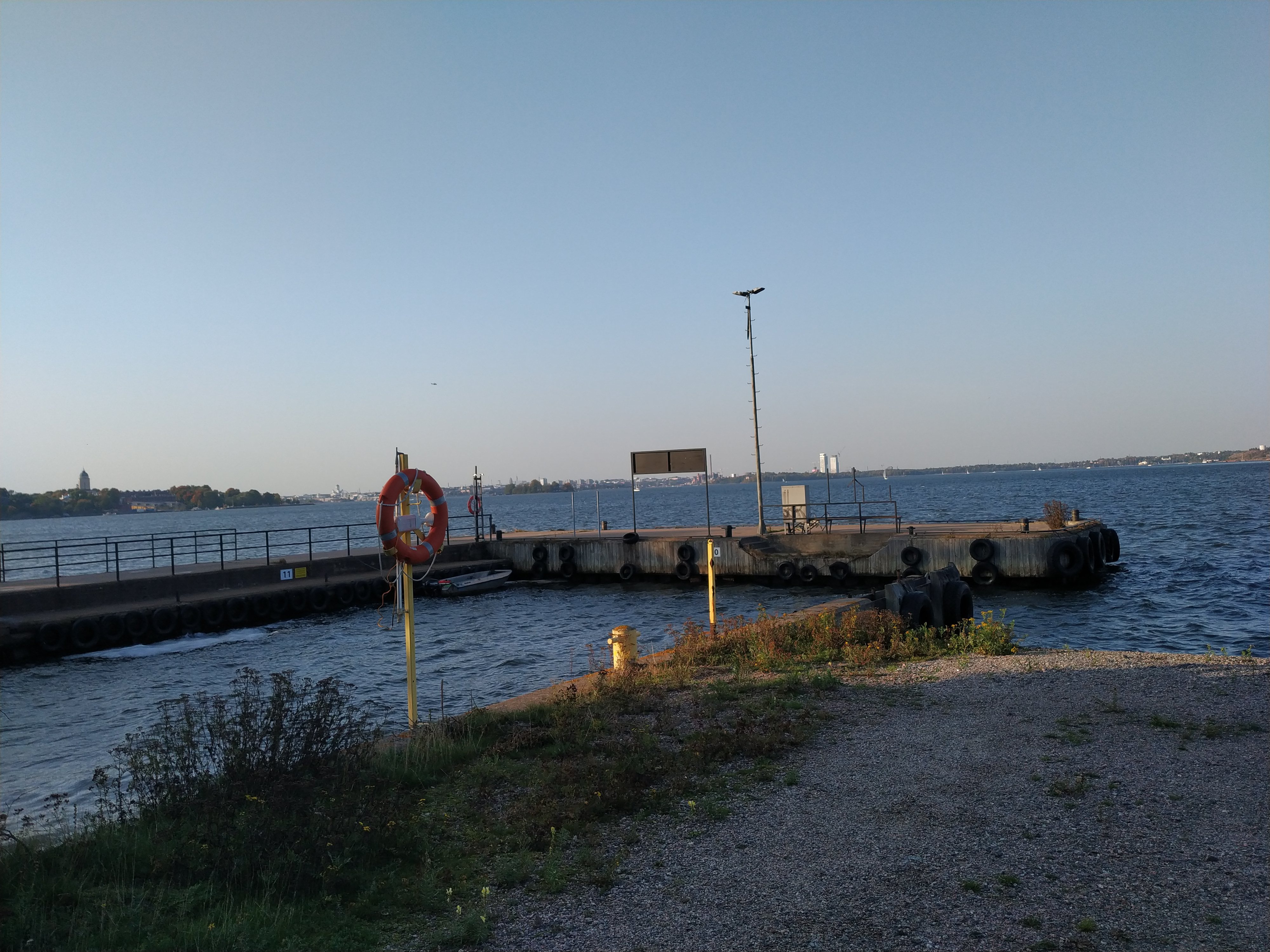 Näkymä Vallisaaren venesatamasta. Etualalla puuveneitä lankuista rakennettuun laituriin kytkettyinä, taustalla betoninen laituri, jonka kainalossa näkyy armeijan yhteysvene YM13. Vallisaari oli pitkään sotilasaluetta, ensin Venäjän armeijan ja Suomen itsenäistymisen jälkeen Suomen armeijan käytössä. Taustalla meren selällä hohtaa risteilijä Statendam. rephoto