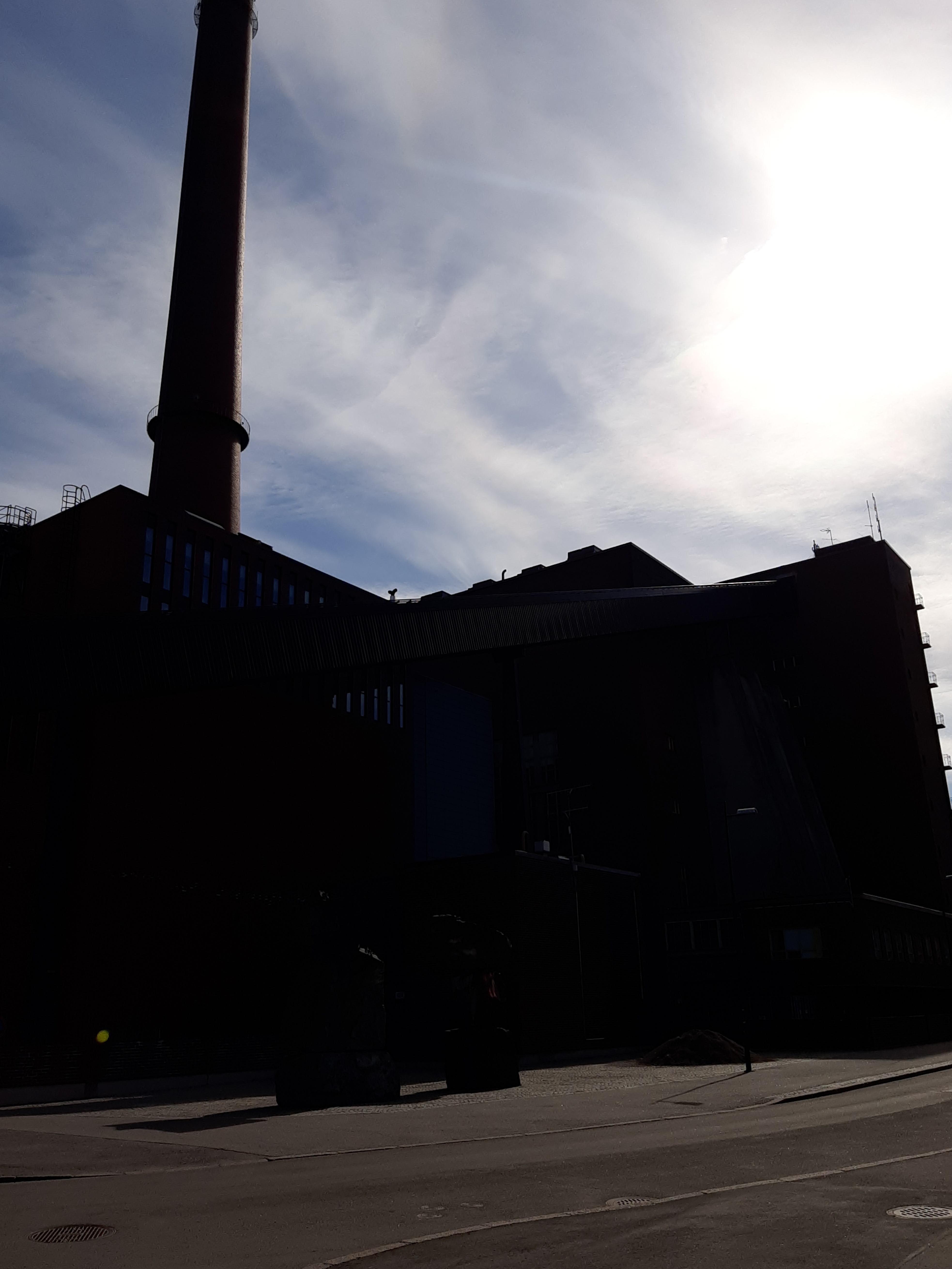 Helsingin sähkölaitoksen Salmisaaren voimala, Lauttasaarenkatu 11 (nyk. Porkkalankatu 9-11), nähtynä Tallberginkaun toiselta puolen, Porkkalankadun pohjoispuolelta. Rakennuksen savupiippu oli valmistuessaan ja pitkään sen jälkeenkin Helsingin korkein. Piipun editse rakennuksen yläkertaan nousee hiiltä polttoaineeksi kuljettava linjasto. Voimala A:n suunnitteli arkkitehti Vera Rosendal kaupunginarkkitehti Hilding Ekelundin johdolla, ja se otettiin käyttöön vuonna 1953. Valokuvan ylänurkissa näkyy kaareutuva tumma varjo, joka johtuu siitä, että valokuvaaja on käyttänyt kuvatessaan vastavalosuojaa. rephoto