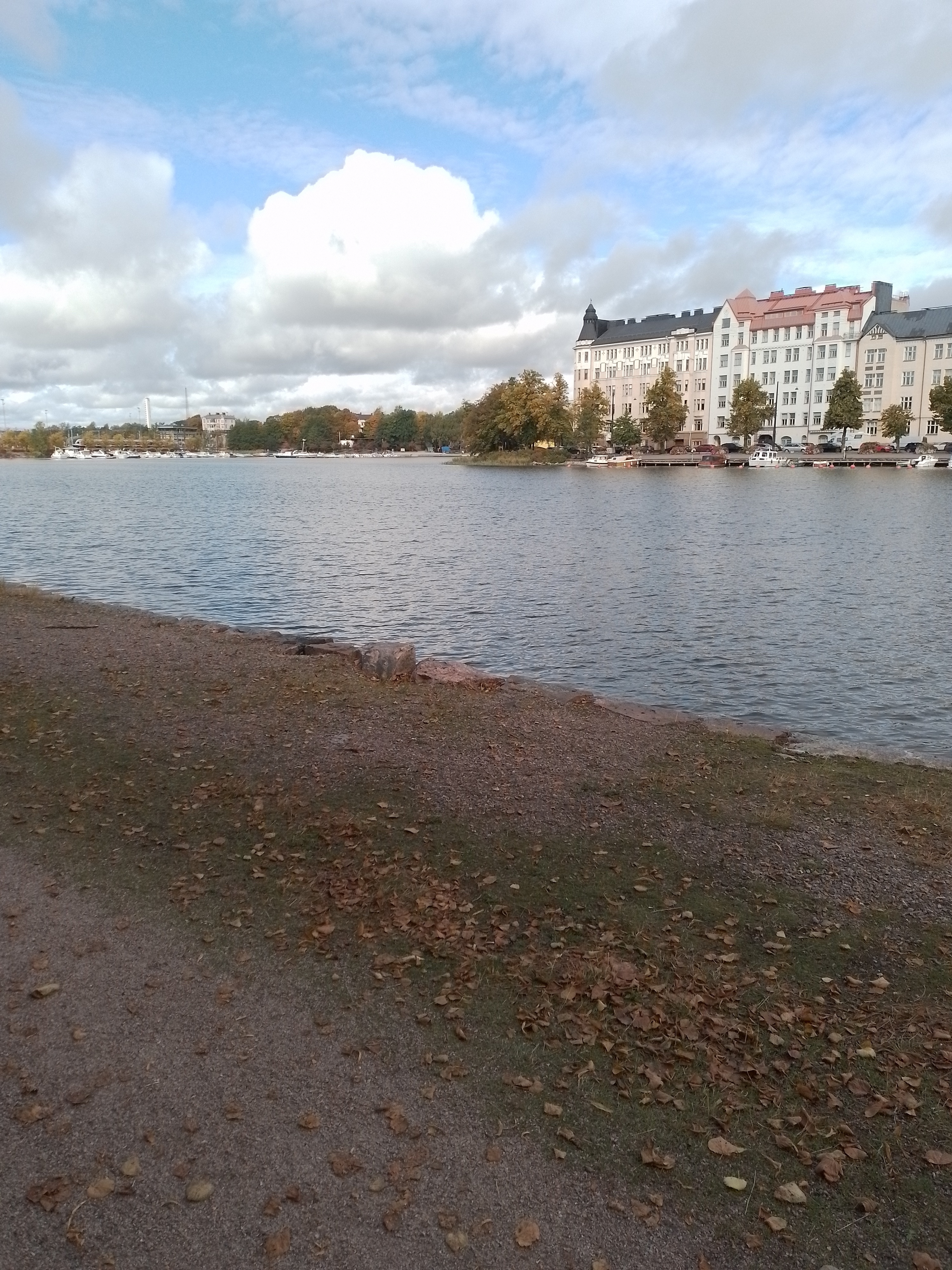 Kolme henkilöä nostamassa venettä Kaisaniemenlahden rannalla. Taustalla Pitkänsillanranta 13 - 17. rephoto