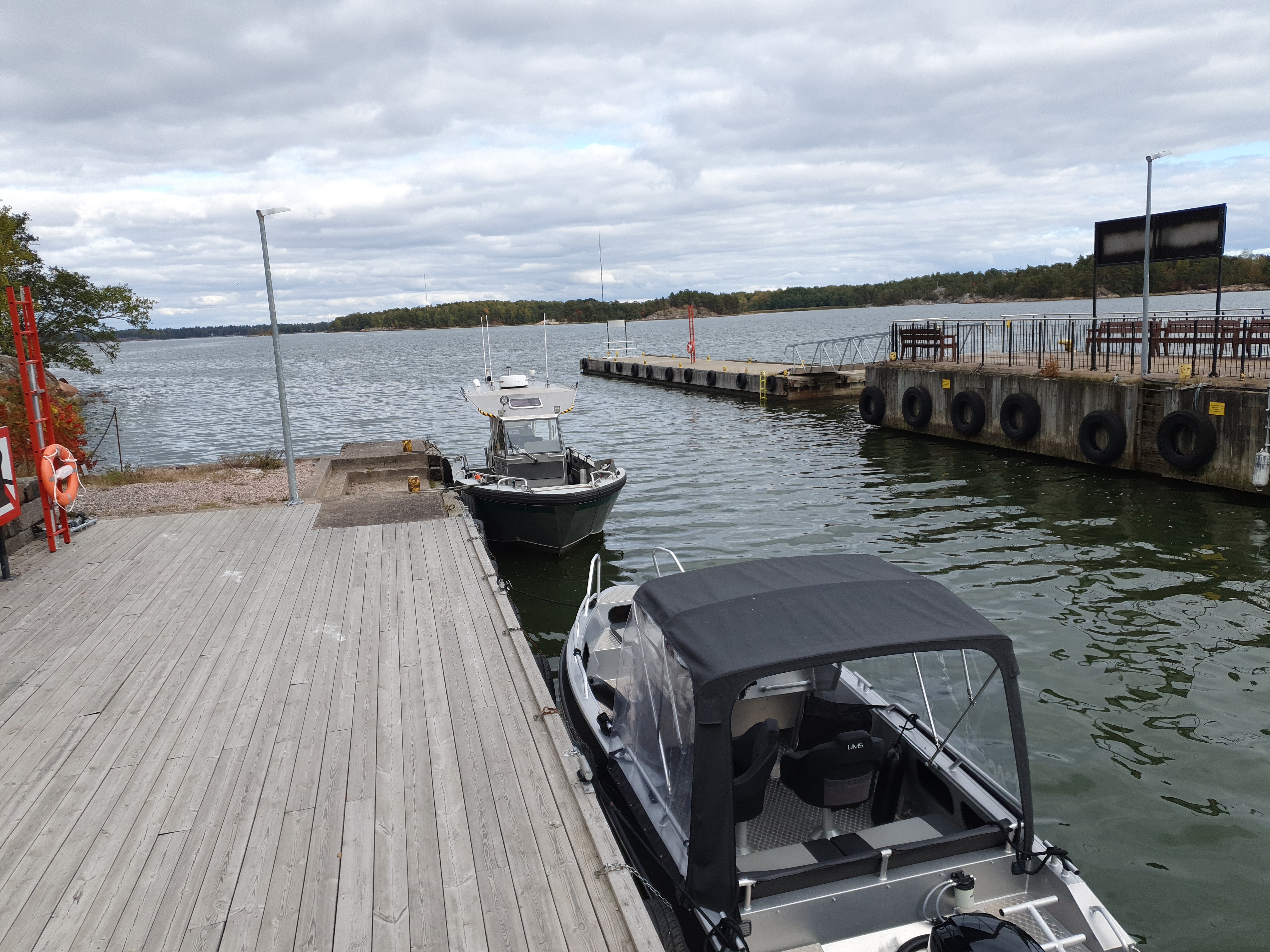 Retkeläiset menossa taksiveneeseen Vallisaaressa. Paikka on Torpedolahden laituri Vallisaaren itärannalla. Taivaanrannassa Haminansalmen toisella puolen näkyy Santahamina. rephoto