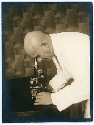 Johannes Vares valges kitlis kummardamas mikroskoobi kohale.  duplicate photo