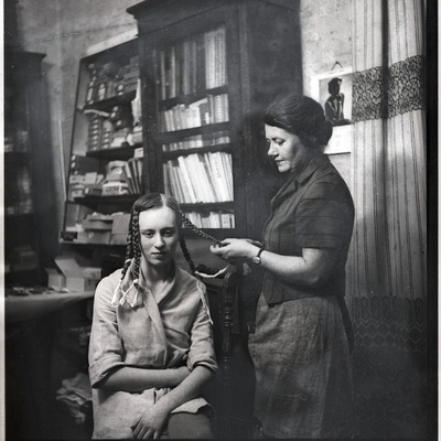 Ethel Malle Sarap ja Johanna Triefeldt toas patse punumas, taustal riiulid karpide ja raamatutega  similar photo