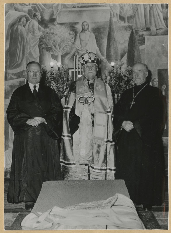 Metropoliit Aleksander seismas koos kahe teise mehega kirikus altari ees