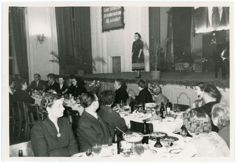 Suure Sotsialistliku Oktoobrirevolutsiooni 40.aastapäeva üritus Sakala keskuses 1958, laval esineja (kõneleja), saalis istuvad inimesed kaetud laudade taga. Ajakirja Nõukogude Naine peatoimetaja Magda Korb istub seljaga lava poole, vasakult kolmas
