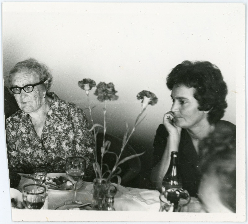 Vilhelmine Klementi õde Marta Schartup ja ta tütar Eva (Part) kaetud laua taga teadmata üritusel istumas, laual vaasis punased nelgid
