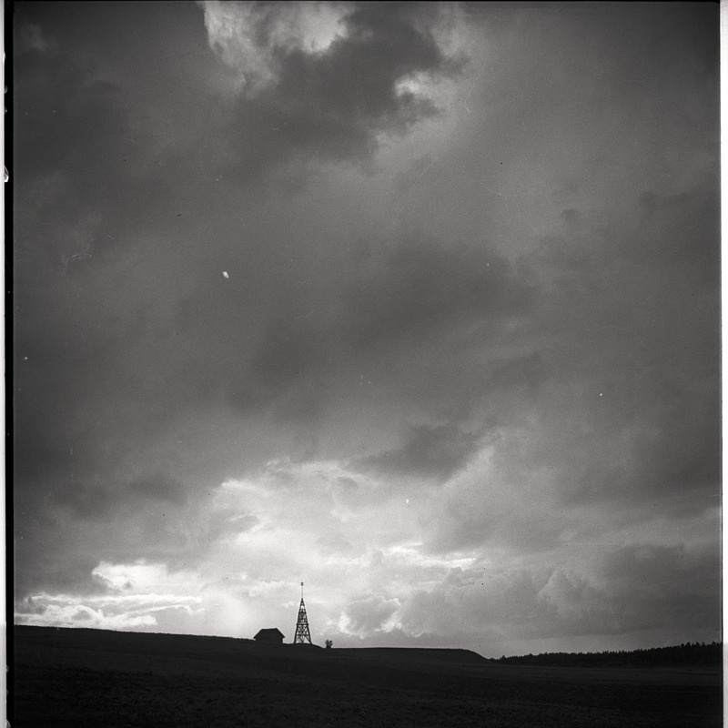 Maastik, tagaplaanil hoone ja puidust torn