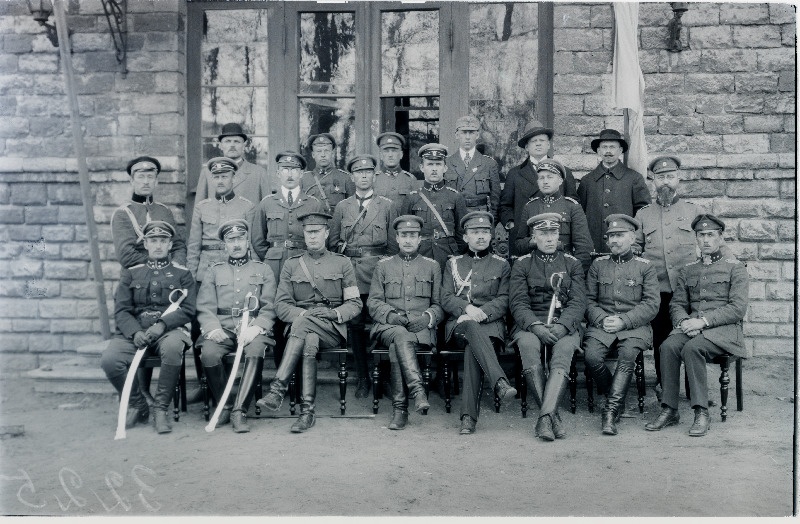 Vabadussõda. Sõjakooli juhtkond, lektorid ja külalised kooli hoone ees Tehnika tänaval. Vasakult: I rida - 1.taktika lektor ja kadettide jalaväeroodu ülem kapten Ludvig Jakobsen, 2.kooli ülem kapten Aleksander Simon, 3.tundmatu Ameerika Ühendriikide ohvitser, 4.sõjaministri abi ja tagavaravägede ülem kindralmajor Andres Larka, 5.Kindralstaabi ülem alampolkovnik Jaan Rink, 6.kooli klasside inspektor alamkapten Heinrich Paavijaan (Hendrik Pallandi), 7.topograafia lektor ja Sõjaväe Korraldusvalitsuse topograafiaosakonna ülem alampolkovnik Eduard Bach, 8.fortifikatsiooni lektor ja Inseneripataljoni ülem kapten Voldemar Riiberg (Rieberg); II rida: 1.kooli adjutant alamleitnant Magnus Siiak, 2.[taktika lektor ja jalaväekadettide 2.rühma ülem alamleitnant Richard Kent], 4.[raadiosidelektor alamleitnant Friedrich Olbrei] 5.kuulipildujate materjalosa lektor ja Kaitseliidu staabi ohvitser leitnant Albert Murrik, 6.lõhkeainete lektor ja Sõjaväe Korraldusvalitsuse inspektorijaoskonna ülem alamkapten August Steinberg, 7.telegraafiside lektor ja Kindralstaabi Valitsuse maakuulamise (luure-) osakonna ülem alamleitnant Arthur Perna (Artur Pärna); III rida: 3 .ratsaklassi ülem kapten Alfons Parisson (Parison), 6.[eesti keele lektor Karl Pinkowski?].