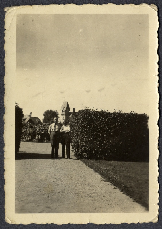 Feliks Siiman ja tundmatu mees seisavad liivatatud teel mingi hoone või hoonekompleksi sissekäigu juures heki kõrval