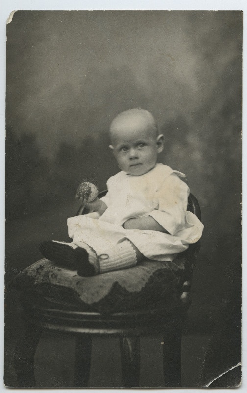 Fotol istub väike laps toolil ja hoiab käes mänguasja [võib olla Endel Tehver]