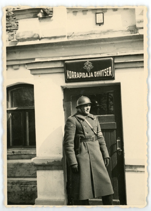 Eesti Vabariigi sõjaväe mundris mees hoone taustal seismas, maja ukse kohal paistab silt "Korrapidaja ohvitser"