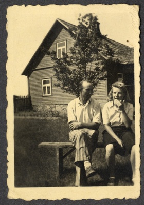 Osvald Asi istub tundmatu naisterahvaga õues pingil, taustal elumaja ja puu  similar photo