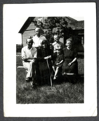 Osvald Asi perekonnafoto: mees, musta rõivastatud vanem naine kepiga, tüdruklaps ja noor naisterahvas istuvad pingil, meesterahvas ja poisslaps seisavad nende taga. Taustal elumaja  similar photo