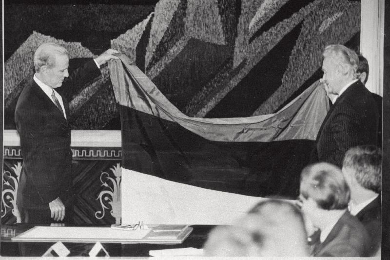 USA riigisekretär James Baker (vasakul) annab Eesti Vabariigi Ülemnõukogu esimehele Arnold Rüütlile üle sini-must-valge lipu, mis seisis pool sajandit USA Riigidepartemangu vestibüülis, kui Eesti annekteerimise mittetunnustamise sümbol.