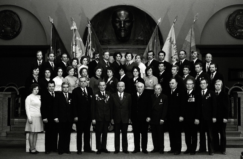 Vabariigi töötajate, sotsialistliku võistluse võitjate pildistamine revolutsiooni-, lahingu -ja töökuulsuse lippude juures Eesti NSV Ministrite Nõukogu valges saalis seoses Suure Sotsialistliku Oktoobrirevolutsiooni 60. aastapäeva tähistamisega, H.Pöögelmanni nimelise Elektrotehnikatehase kontrolörid Zinaida Metus, Galina Kukuškina, Mare Tutt, liimija Ljubov Žiglova, segude ja lahustite valmistaja Eeva Kroon, tehniliste seadmete korrastaja Petr Matijanko, operaator Asta Vaher, tsehhiülem Voldemar Raag, bürooülem Aleksandr Striz, direktor Toivo Ufert; tootmiskoondise RET siduja, Eesti NSV teeneline tööstustöötaja Jekaterina Lentsman, monteerija Larissa Maljutina,  jätkub: elektrikeevitaja Aleksandr Treier, reguleerija Aleksandr Kutškudon, osakonnaülem Ideja Rapoport,tööline Malle Luker, lukksepp Vadim Strelkov, peadirektor Petr Melnik; A. Veimeri nimelise Võru Gaasianalüsaatorite Tehase treial Rein Sendik, töölised Liidia Verro ja Vambola Soorrits, lukksepp