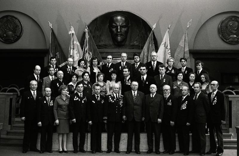 Vabariigi töötajate, sotsialistliku võistluse võitjate pildistamine revolutsiooni-, lahingu - ja töökuulsuse lippude juures Eesti NSV Ministrite Nõukogu valges saalis seoses Suure Sotsialistliku Oktoobrirevolutsiooni 60. aastapäeva tähistamisega, M.I. Kalinini nimelise Elektrotehnika Tehase lukksepad Mihhail Mihhailov, Enn Ehala, Gavruša Galstjan, Sulo Lal, brigadir Boris Moronov, lihvija Niina Skvortsova, söövitajad Tamara Snezitskaja, Ljudmila Veremei ja Tatjana Samus, osakonnajuhataja Aleksei Hõbemägi; tehase Volta stantsija Nadežda Ojasaar, isolatsiooni valmistaja Jefrosinja Podoroznaja, maaler Klaudia Berdinskih,  jätkub: töölised Evald Vainumaa ja Veno Tšistogradov, lukksepp-monteerija Galina Matjušina, tõstukijuht Anatoli Pavlov, tehase Estoplast brigadir Aino Sipp, galvaanik Enn Ehasalu, monteerija Helve Toajaak; tehase Eesti Kaabel tööline Elmar Ojaste, pressija Linda Nagel; Eesti Soojuselektrijaama Ehitusvalitsuse maaler Niina Kotšneva, meister Anna And