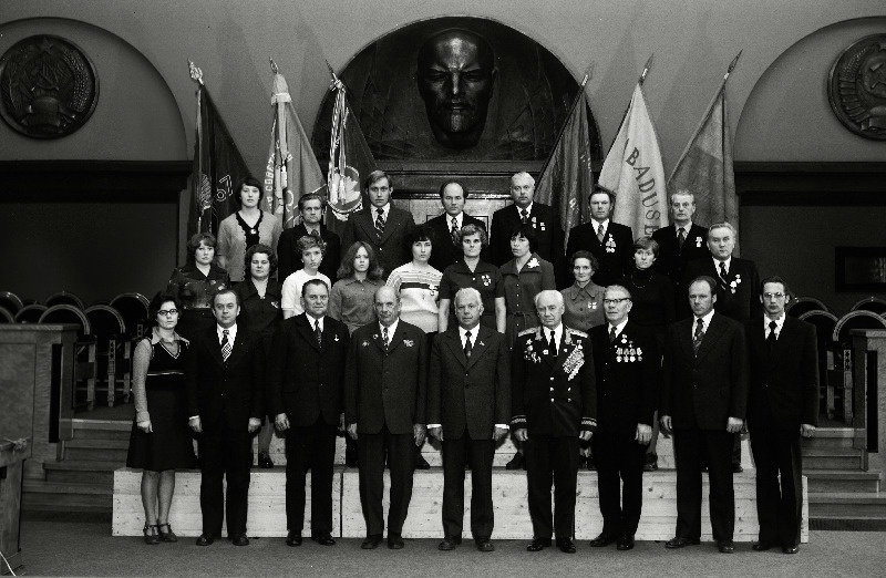 Sidetöötajate, sotsialistliku võistluse võitjate pildistamine revolutsiooni-, lahingu- ja töökuulsuse lippude juures Eesti NSV Ministrite Nõukogu Valges saalis seoses Suure Sotsialistliku Oktoobrirevolutsiooni 60. aastapäeva tähistamisega. Pärnu Rajooni Sidesõlme ülem Endel Tuisk, Vabariikliku Televisiooni Saatekeskuse vaneminsener Mati Tähemaa, Tallinna Kesktelegraafi telegrafist Aino Viigimäe, Viljandi Rajooni Sidesõlme operaator Ene Ilves, Rakvere Rajooni Sidesõlme operaator Taimi Kurg, Tallinna Peapostkontori operaator Katrin Lee, Pärnu Rajooni Tõstamaa Sidesõlme ülem Leopold Lõpp,    jätkub: Kohtla-Järve Rajooni Sidesõlme postiljon Galina Merkulova, Pärnu Ekspluatatsiooni - Tehnilise Sidesõlme elektrimontöör Tiit Metsallik, Harju Rajooni Sidesõlme telefonist Marika Raiend, Narva Linna Sidesõlme telefonist Antonina Rubanova, Paide Rajooni Sidesõlme operaator Elvi Saad, Ajakirjanduslevi Pärnu Rajooni agentuuri kiosköör Asta Sukk, Kingissepa Rajooni